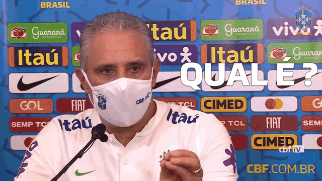 a man wearing a face mask is speaking into a microphone in front of a sign that says quale