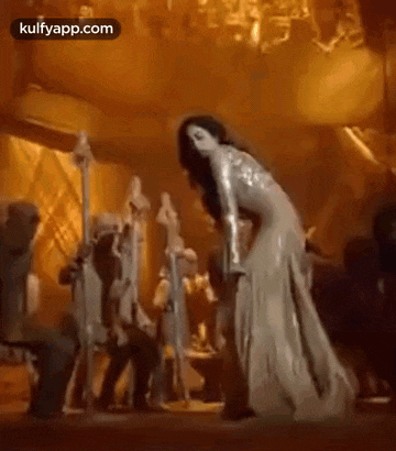 a woman in a long dress is dancing in front of a crowd .