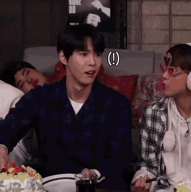 a group of people are sitting around a table with a cake and a poster that says kunz do on the wall behind them