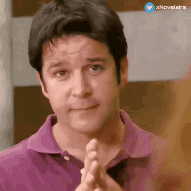 a man in a purple shirt is clapping his hands in front of his face
