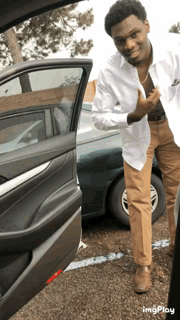 a man in a white shirt and khaki pants is standing in front of a car with the word imgplay on the bottom