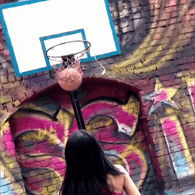a woman is playing basketball in front of a graffiti wall