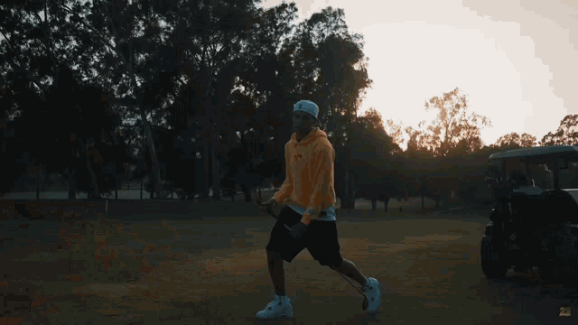 a man wearing a yellow hoodie and a white hat is holding a golf club in a park
