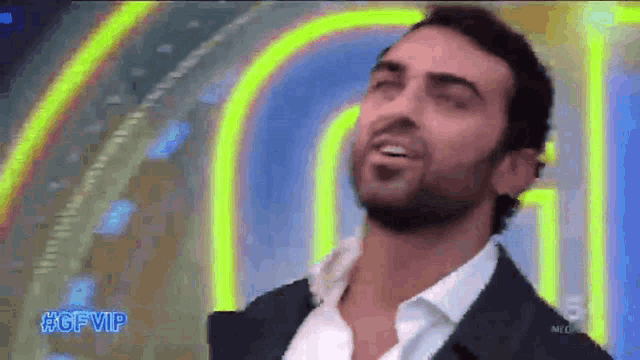 a man in a suit and white shirt is standing in front of a neon sign .