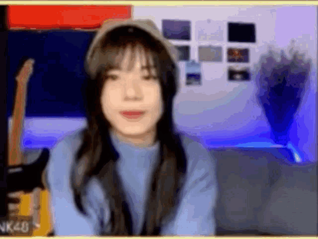 a woman in a blue sweater and hat is holding a guitar in front of a camera .
