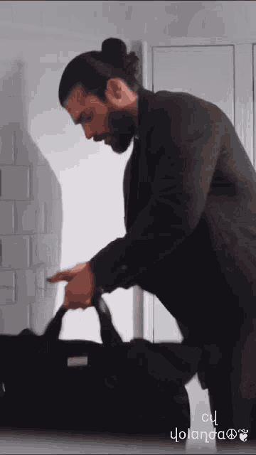 a man in a suit is holding a black bag and pointing at it .