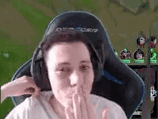 a man wearing headphones is sitting in a gaming chair and covering his mouth .