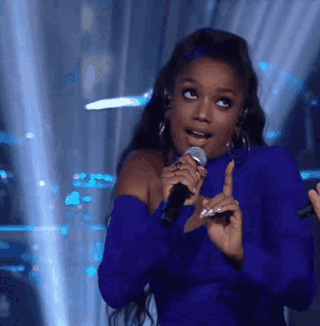 a woman in a blue dress is singing into a microphone on stage