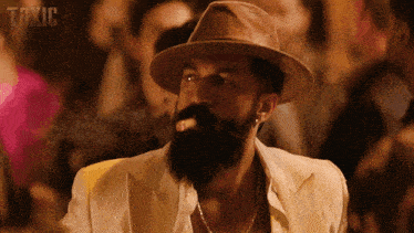 a man with a beard wearing a hat is smoking a cigar with the word toxic behind him