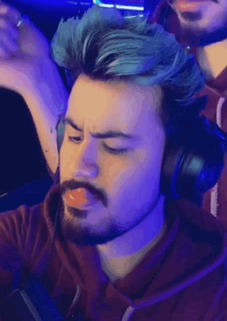 a man with blue hair and a beard wearing headphones and a pacifier in his mouth .