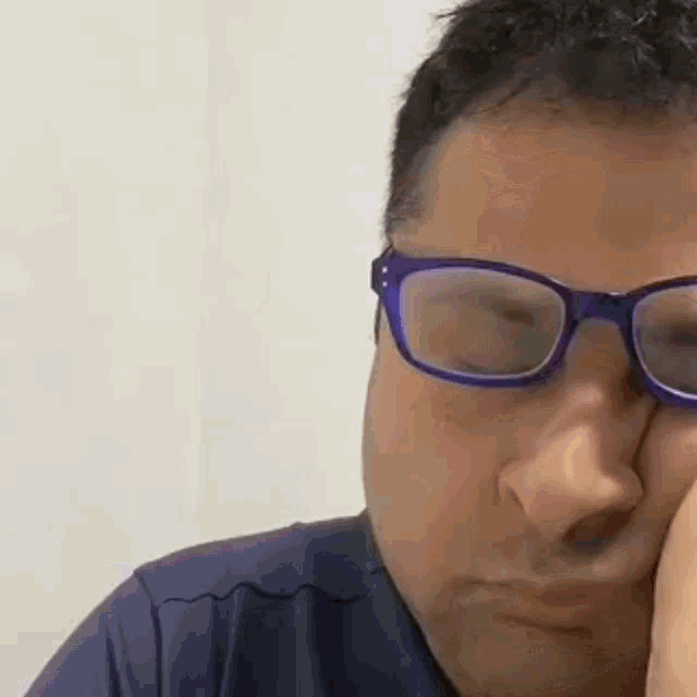 a man wearing glasses is rubbing his face .