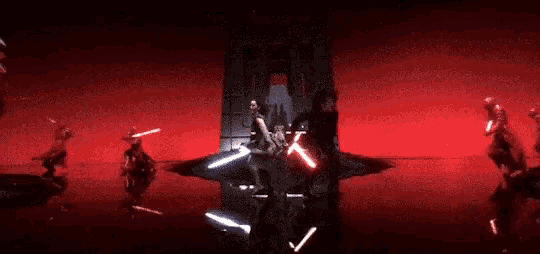 a group of people are standing in a dark room with lightsabers in their hands .