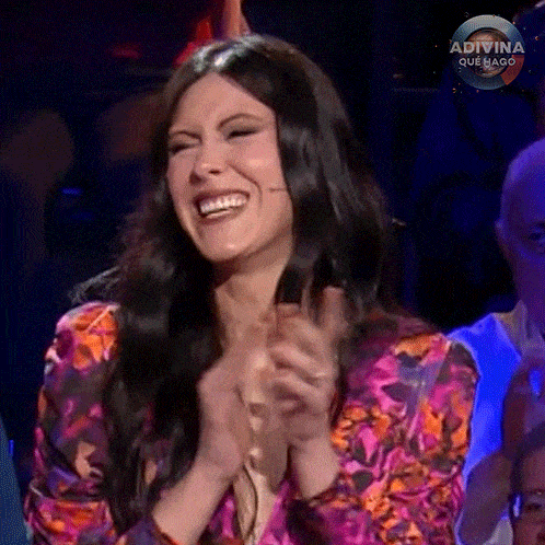 a woman is laughing and clapping her hands while sitting in a crowd .