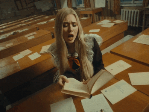 a woman is sitting at a desk reading a book with her mouth open