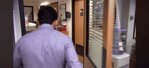 a man in a purple shirt is walking into a room with a water cooler