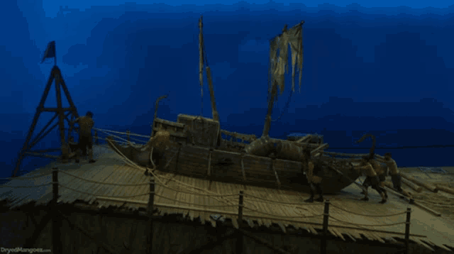 a group of men are pulling a boat on a raft with the words dryedmangoes.com visible in the corner