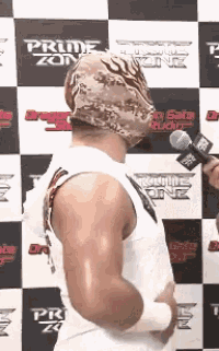 a man wearing a mask is being interviewed by a man with a microphone in front of a wall that says prime zone