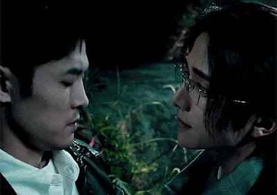 a man wearing glasses looks at another man in a dark room
