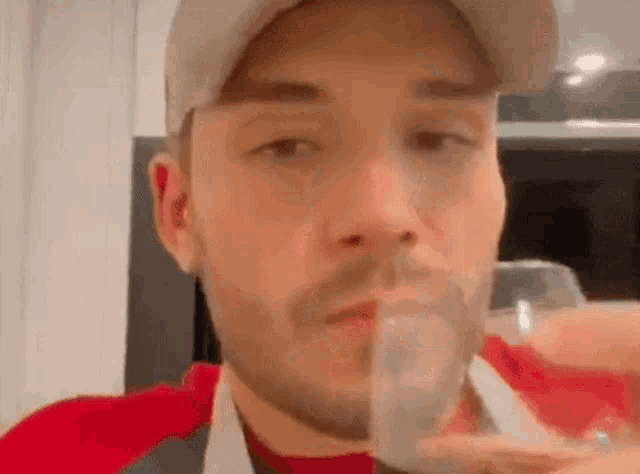 a man with a beard is drinking from a glass while wearing a hat .