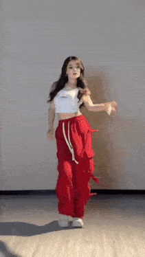 a woman in a crop top and red pants is dancing on a wooden floor .