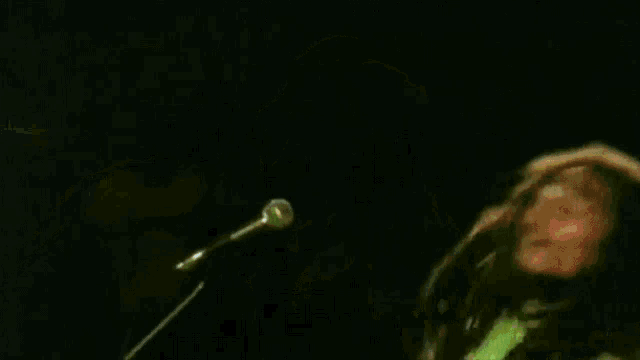 a man in a green shirt is singing into a microphone on a stage .