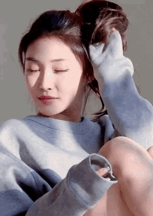 a woman wearing a grey sweatshirt holds her hair up in a bun