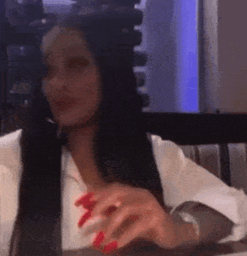 a woman is sitting at a table in a restaurant with red nails and a white shirt .