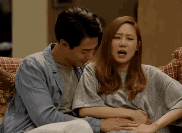 a man and a woman are sitting on a couch and the woman is holding the man 's stomach