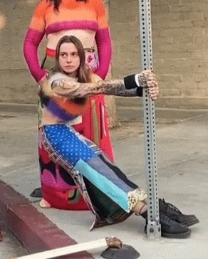 a woman with tattoos on her arm is kneeling down next to a pole