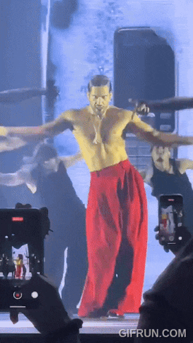 a shirtless man in red pants is being photographed by a phone with gifrun.com at the bottom