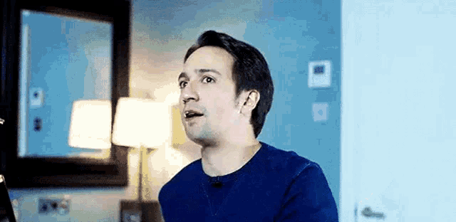 a man in a blue shirt is sitting in front of a computer in a room .