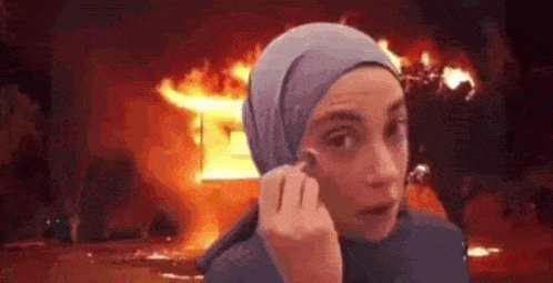 a woman in a hijab is talking on a cell phone in front of a fire .