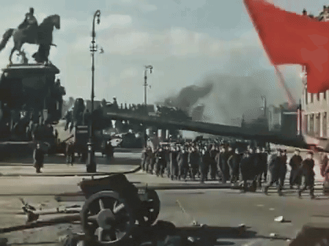 a statue of a man riding a horse is behind a crowd of people walking down a street