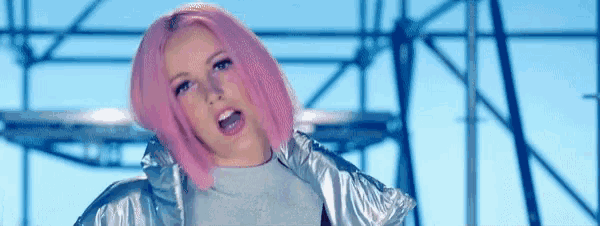 a woman with pink hair and a silver jacket stands in front of a blue sky