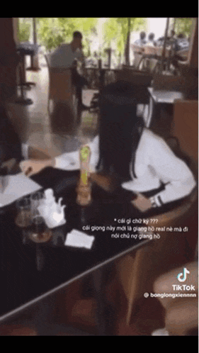 a woman is sitting at a table in a restaurant looking at her phone .