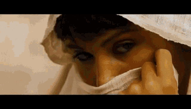 a close up of a woman covering her face with a white scarf .