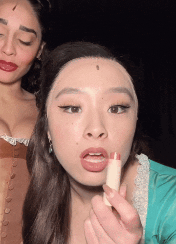 a woman is putting lipstick on another woman 's lips