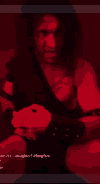 a man in a black outfit is sitting in a dark room with a red background
