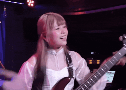 a woman in a white shirt is playing a guitar in a dark room