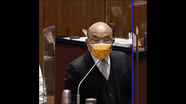 a bald man in a suit and tie is speaking into a microphone in front of a chinese sign