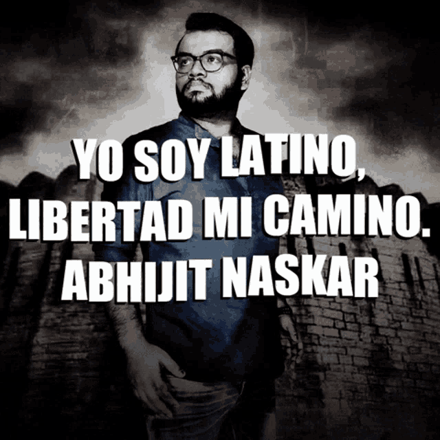 a man with glasses stands in front of a brick wall with the words yo soy latino libertad mi camino abhijit naskar