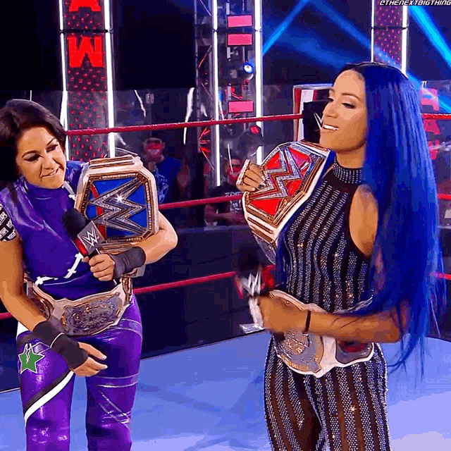 a woman with blue hair is holding a wwe championship belt next to another woman