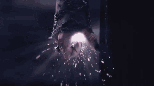a close up of a fist with sparks coming out of it in a dark room .