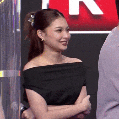 a woman wearing a black off the shoulder top smiles