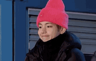 a young man wearing a pink beanie and a black jacket is standing in front of a blue door .