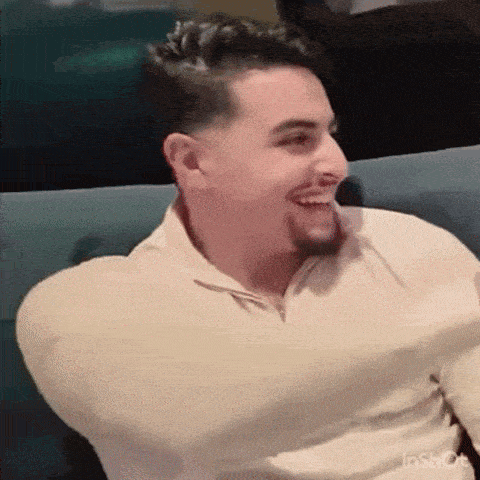 a man is sitting on a couch laughing with his arms outstretched .