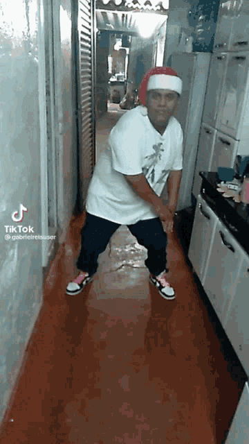 a man wearing a santa hat and a white shirt is dancing in a kitchen