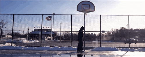 a person standing in front of a basketball hoop with an american flag flying in the background