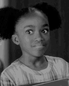 a little girl is holding a book and making a funny face in a black and white photo .