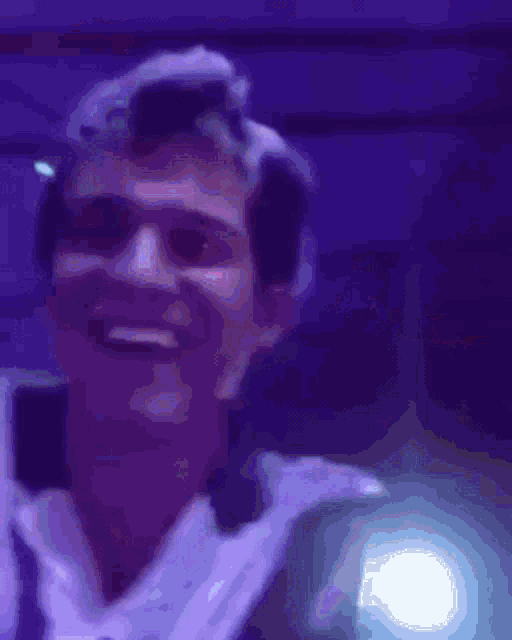 a man in a tuxedo is laughing in a dark room with a purple background .